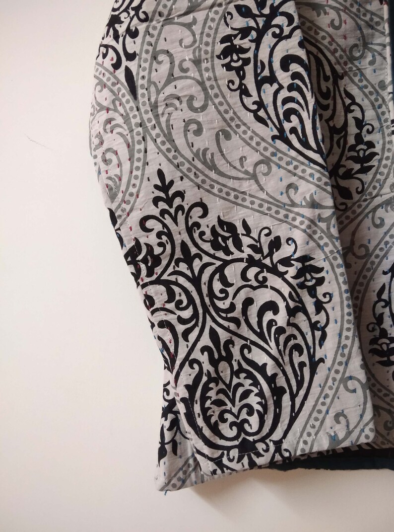 K&ouml;nnte beinhalten: Nahaufnahme eines grauen und schwarzen Stoffes mit Paisley-Muster. Der Stoff hat eine gesteppte Textur und ist umgeklappt.