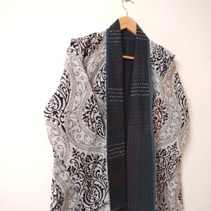 K&ouml;nnte beinhalten: Ein Kimono mit schwarz-wei&szlig;em Muster und einer blaugr&uuml;nen Futter. Der Kimono h&auml;ngt an einem Holzb&uuml;gel.