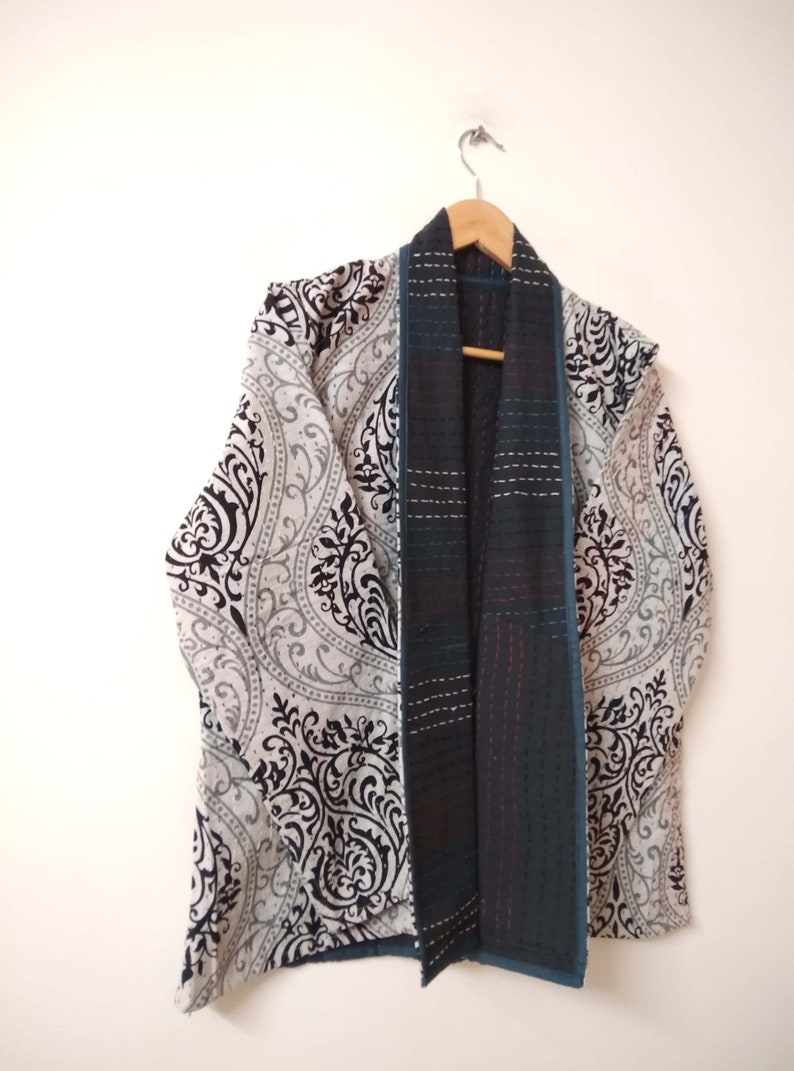 K&ouml;nnte beinhalten: Ein Kimono mit schwarz-wei&szlig;em Muster und einer blaugr&uuml;nen Futter. Der Kimono h&auml;ngt an einem Holzb&uuml;gel.