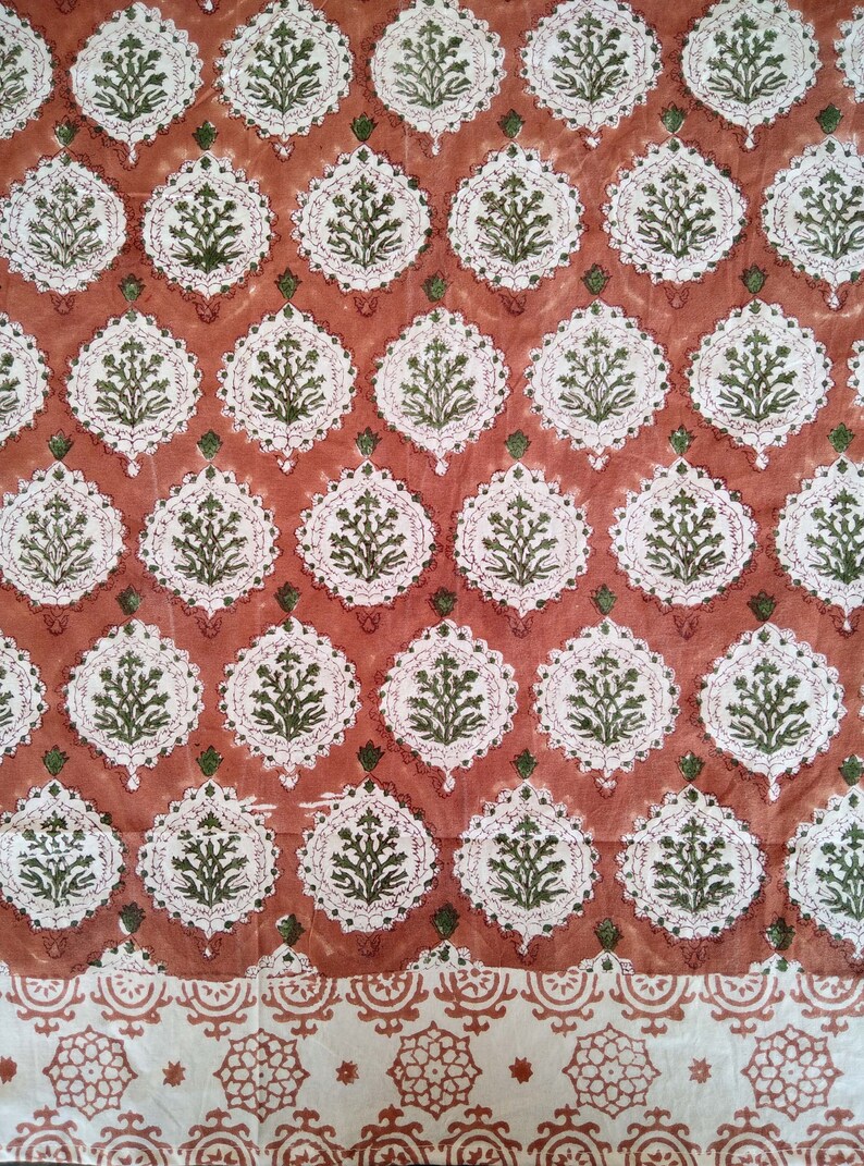 Pu&ograve; includere: Un tessuto rosso con un motivo floreale bianco e verde. Il tessuto ha un bordo con un motivo simile su scala pi&ugrave; piccola.