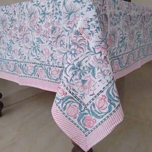 Peut inclure: Une nappe blanche avec un motif floral rose et vert. La nappe a une bordure ray&eacute;e rose et blanche.