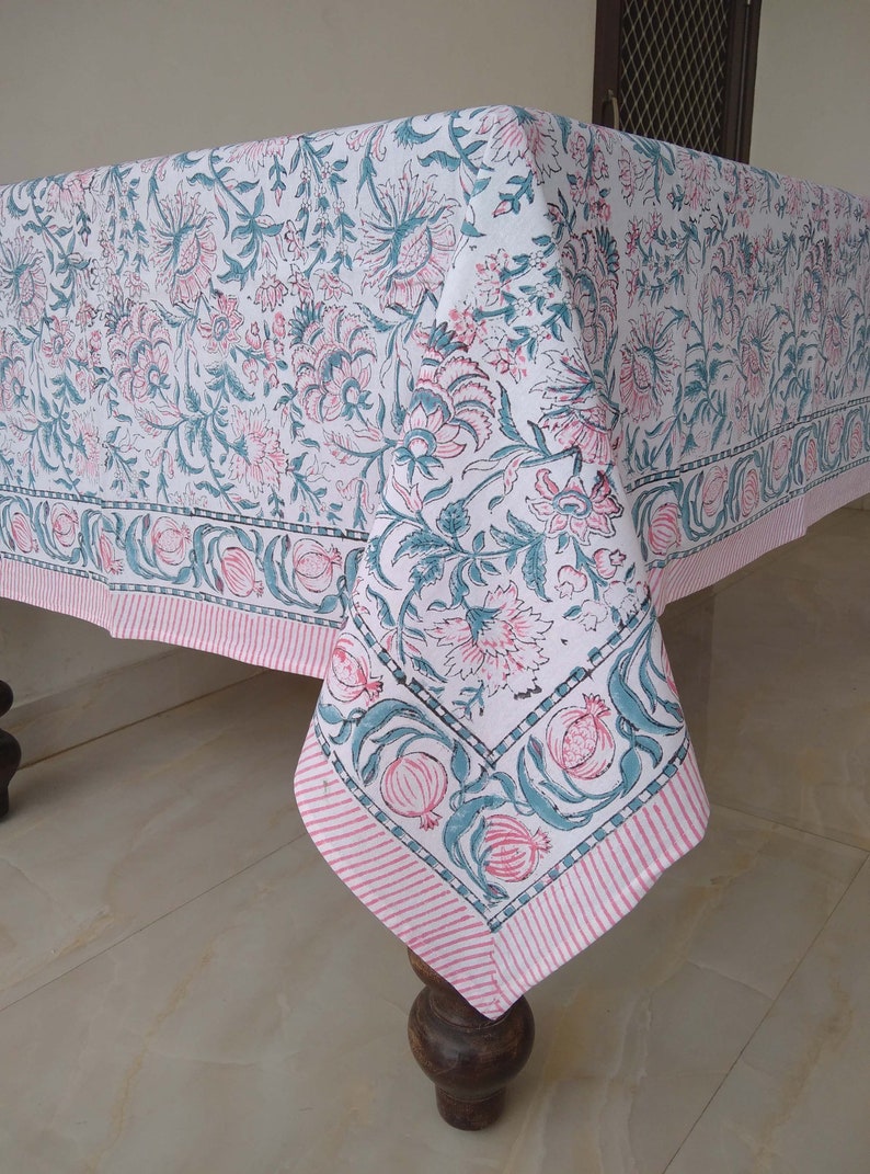 Peut inclure: Une nappe blanche avec un motif floral rose et vert. La nappe a une bordure ray&eacute;e rose et blanche.