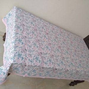 Peut inclure: Une nappe blanche avec un imprim&eacute; floral rose et vert. La nappe a une bordure rose et est drap&eacute; sur une table en bois.