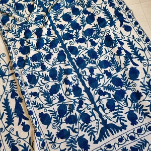 May include: A white fabric tablecloth with a blue embroidered design of a tree with leaves and fruit. The design is intricate and detailed, and the colours are vibrant.