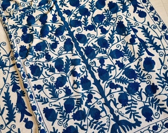 Puede incluir: Un mantel de tela blanco con un diseño bordado azul de un árbol con hojas y frutos. El diseño es intrincado y detallado, y los colores son vibrantes.