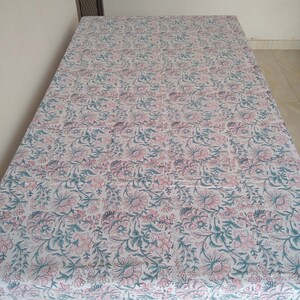 Peut inclure: Une nappe blanche avec un motif floral rose et vert. La nappe a une bordure ray&eacute;e rose et blanche.