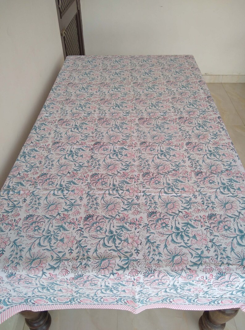 Peut inclure: Une nappe blanche avec un motif floral rose et vert. La nappe a une bordure ray&eacute;e rose et blanche.