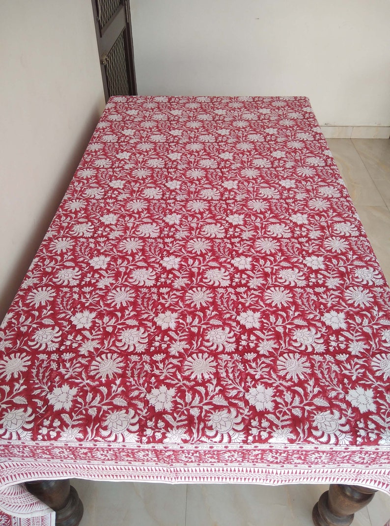 K&ouml;nnte beinhalten: Eine rote und wei&szlig;e Tischdecke mit Blumenmuster und wei&szlig;em Rand. Die Tischdecke ist aus Baumwolle und hat ein traditionelles indisches Design.