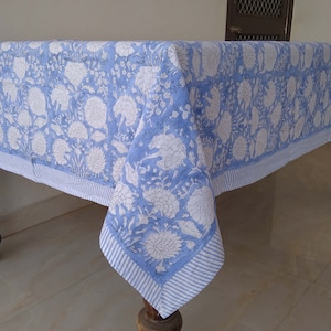 May include: A blue and white floral tablecloth with a striped border. The tablecloth is draped over a wooden table with turned legs.