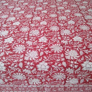 K&ouml;nnte beinhalten: Rotes Baumwoll-Bettlaken mit wei&szlig;em Blumenmuster. Das Laken hat einen Rand mit einem wei&szlig;en und roten geometrischen Muster.