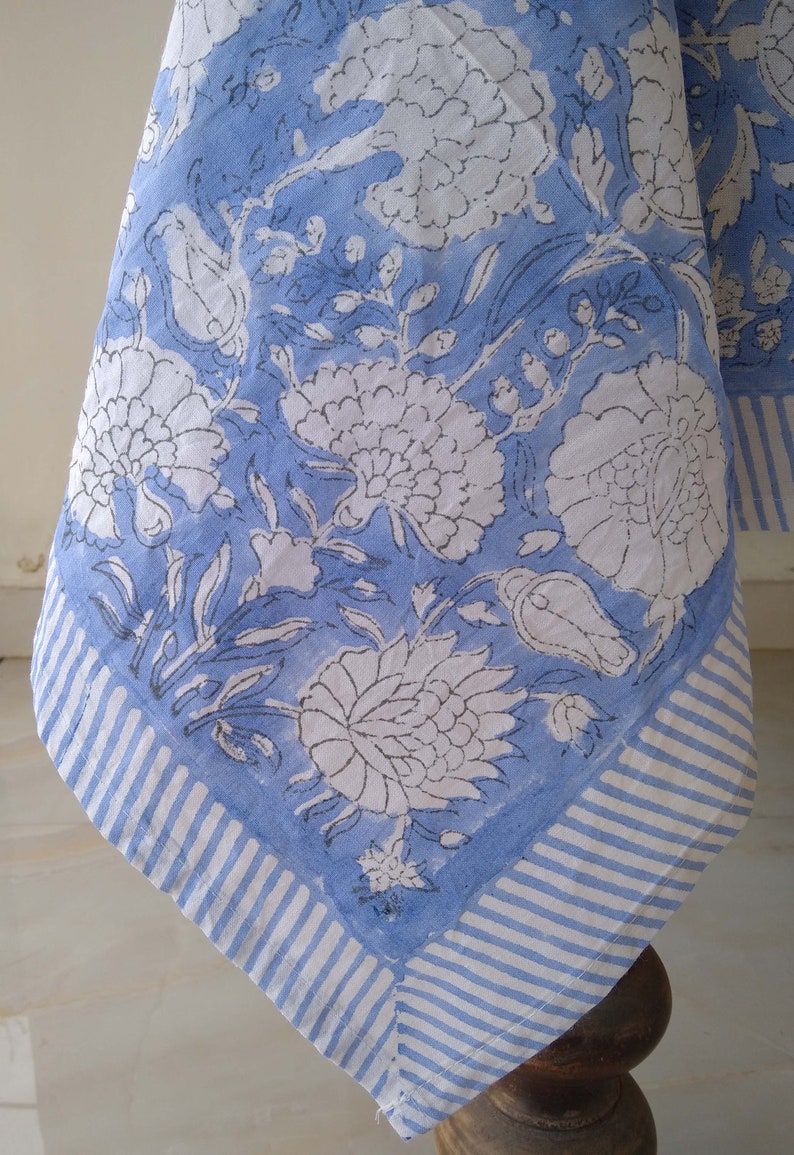 May include: A blue and white tablecloth with a floral pattern. The tablecloth has a white border with blue stripes.