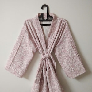 Puede incluir: Una bata de color rosa y blanco con estampado, cinturón de atar y mangas largas.
