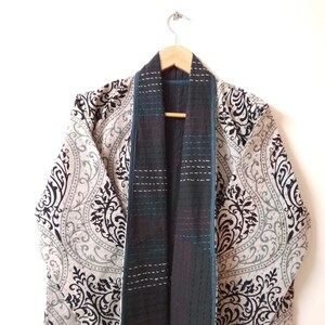 K&ouml;nnte beinhalten: Ein Kimono mit schwarz-wei&szlig;em Muster und einer gesteppten Innenfutter in Tealblau und Schwarz. Der Kimono h&auml;ngt an einem Holzb&uuml;gel.