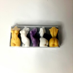 Puede incluir: Cinco peque&ntilde;as figuras esculpidas de torsos humanos en un paquete de pl&aacute;stico transparente. Las figuras est&aacute;n dispuestas en fila y est&aacute;n hechas de un material liso y ceroso. Los colores son amarillo, blanco, morado, blanco y amarillo.