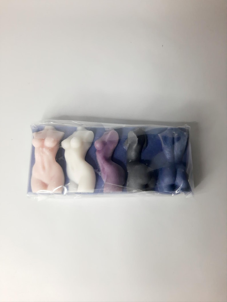 Puede incluir: Cinco peque&ntilde;as figuritas de cera de color vivo con forma humana. Las figuritas est&aacute;n dispuestas en fila sobre un fondo azul. Las figuritas son rosa, blanca, morada, gris y azul.