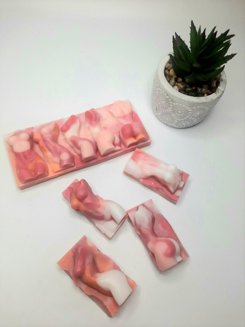 Puede incluir: Cinco barras de jab&oacute;n rosa y blanco con forma de figuras humanas. Las barras de jab&oacute;n est&aacute;n dispuestas en fila sobre una superficie blanca.