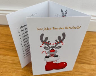 May include: A white, folded Christmas-themed card with a cartoon reindeer wearing a red boot. The reindeer has antlers decorated with red lights and a candy cane. The text "Löse jeden Tag eine Rätselzeile!" is printed on the card.