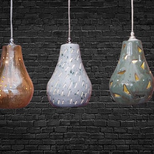 May include: Three ceramic pendant lights in different colours and patterns. The first light is brown with gold dots, the second is light blue with white lines, and the third is green with gold triangles.