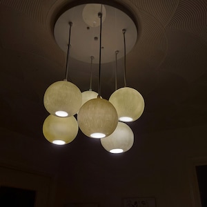 May include: A ceiling light fixture with six round, off-white, textured light shades hanging from a white circular base.