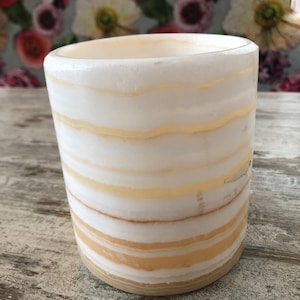 Könnte beinhalten: Weißer Alabaster-Kerzenhalter mit einem gestreiften Muster in Creme- und Beigetönen. Der Halter ist zylindrisch und hat eine glatte, polierte Oberfläche.