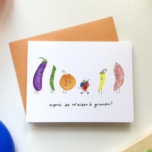May include: A white card with a colorful illustration of vegetables and a small person. The text on the card reads "merci de m'aider &agrave; grandir!"
