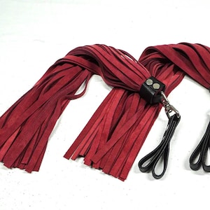 Pode incluir: Dois chicotes de couro vermelho com alças de couro preto e ferragens de metal prateado.