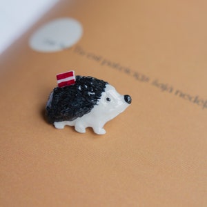 May include: A small white and black ceramic hedgehog figurine with a red and white striped flag on its back.