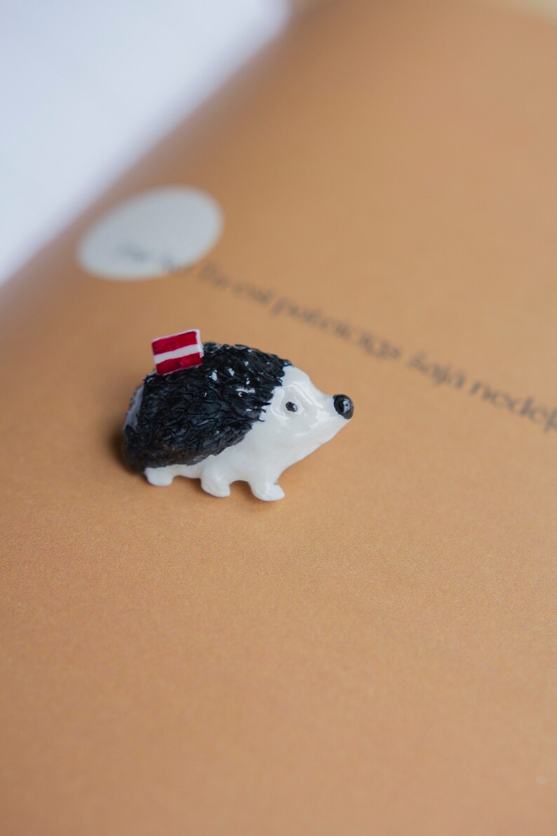 May include: A small white and black ceramic hedgehog figurine with a red and white striped flag on its back.