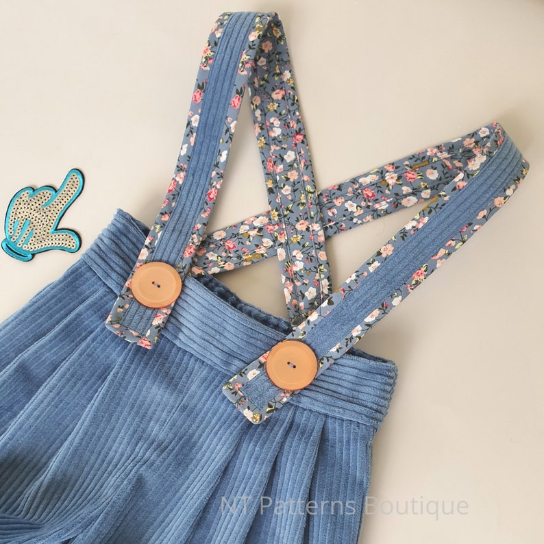 May include: Blue corduroy overall shorts with floral print straps and wooden buttons.  The straps are crossed in the back.  NT Patterns Boutique.