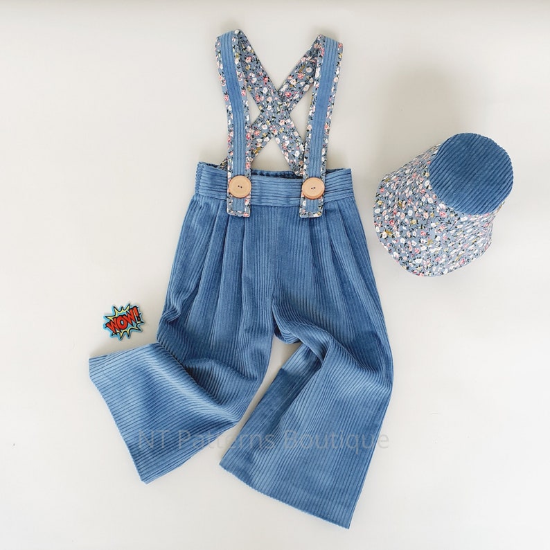 May include: Blue corduroy overalls with floral print straps and wooden buttons. The overalls are paired with a matching blue floral print bucket hat.