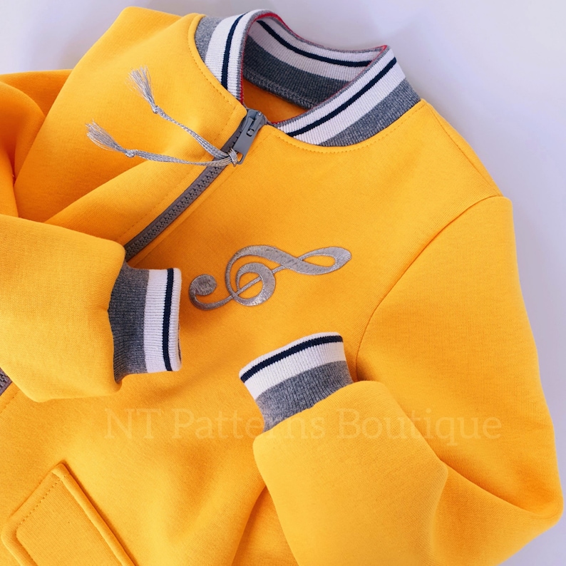 May include: A yellow bomber jacket with a silver musical note design and grey and white striped trim on the collar and cuffs.