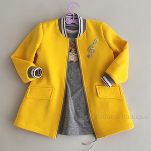 May include: A yellow bomber jacket with a zipper closure and a gray t-shirt with an owl graphic. The jacket has a white stripe on the collar and cuffs. The jacket has a musical note embroidered on the front. The t-shirt has the text "Patterns Boutique" on the bottom.