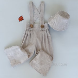 May include: A beige corduroy overall with suspenders and two wooden buttons. The overall has wide legs and comes with a matching beige corduroy bucket hat.