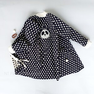 May include: Black and white polka dot dress with a panda bear applique. The dress has a white collar and long sleeves.