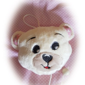 Könnte beinhalten: Weißer Plüschbärenkopf mit gestickten Augen, Nase und Mund. Der Bär ist an einer weißen Schnur mit einer weißen Perle am Ende befestigt.