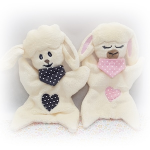 以下が含まれることがあります： 刺繍された顔とハートが付いた、白いぬいぐるみラムの玩具が2つ。1つのラムは黒と白のドット柄のスタイ、もう1つのラムはピンクと白のドット柄のスタイをしています。