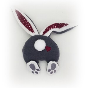 May include: A grey plush bunny with white feet and a white tail. The bunny has red ears with white polka dots and a small red heart on its back.