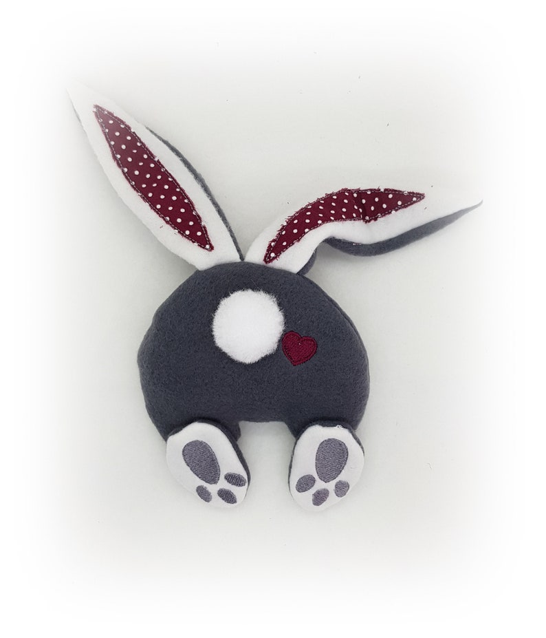 May include: A grey plush bunny with white feet and a white tail. The bunny has red ears with white polka dots and a small red heart on its back.