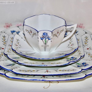 May include: A vintage white teacup, saucer, and plates set with a blue floral design. The set includes a teacup, a saucer, and three square plates. The edges are trimmed with a blue border. The teacup has a blue floral design.