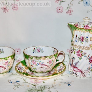 May include: A vintage tea set comprising a teacup, saucer, sugar bowl, and coffee pot. The set is white with a green border and floral and bird patterns. The teacup and coffee pot have gold detailing.