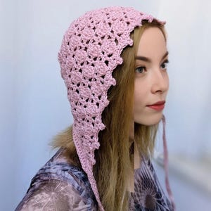 May include: A pink crocheted bonnet with long ties. The bonnet has a scalloped edge and a delicate floral pattern.