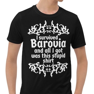 May include: Black t-shirt with white text that reads "I survived Barovia and all I got was this stupid shirt." The text is framed by decorative flourishes. The shirt is short-sleeved and appears to be made of a soft material.