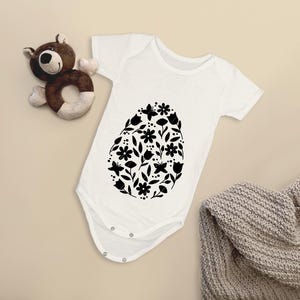 Puede incluir: Un body blanco para beb&eacute; con un dise&ntilde;o floral negro en forma de huevo.