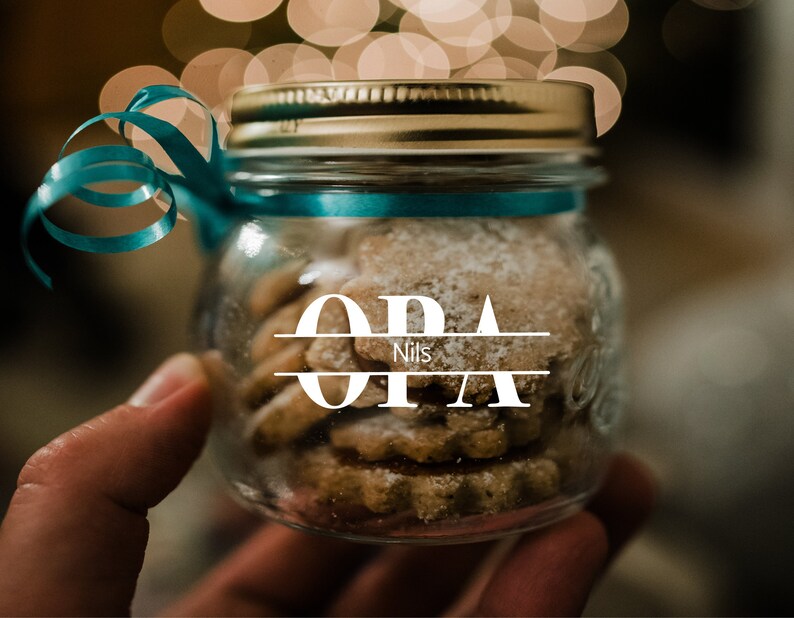 May include: A glass jar with a gold lid and a blue ribbon tied around it. The jar is filled with cookies and has a white label with the text "OPA Nils" on it.