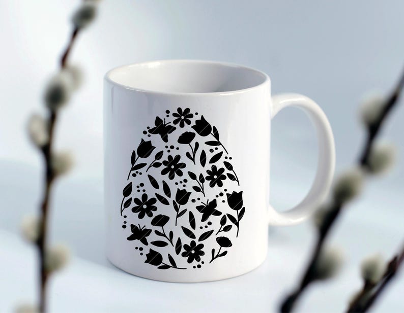 Puede incluir: Taza de cer&aacute;mica blanca con una silueta negra de un dise&ntilde;o en forma de huevo lleno de flores y mariposas.