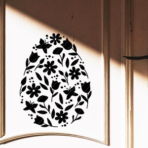 Puede incluir: Una silueta negra de un huevo de Pascua con un dise&ntilde;o floral. El huevo est&aacute; lleno de flores, hojas y mariposas.