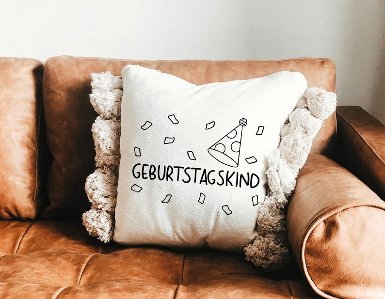 May include: A white throw pillow with a black and white illustration of a party hat and confetti. The text "Geburtstagskind" is printed on the pillow.