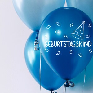 May include: Three blue balloons with a white party hat and the text "Geburtstagskind" on one balloon.