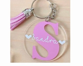 May include: Pink acrylic keychain with a large letter S and the name "Sandra" written in white cursive. The keychain has a pink tassel attached to the metal ring.