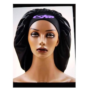 Pode incluir: Um gorro de dormir de cetim preto com um logotipo roxo que diz "S.K.P."